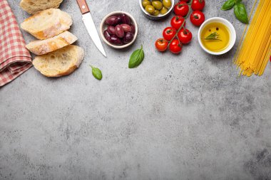 Dilimlenmiş ciabatta, zeytin yağı, spagetti, taze fesleğen, kirazlı domatesler ve gri betondan kırsal arka plan manzarası, fotokopi alanı. İtalyan mutfağı kavramı