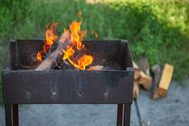 Yakacak odunlu Rustik Metal Barbekü Izgarası. Yeşil bahçede yaz pikniğinde barbekü için alevler..