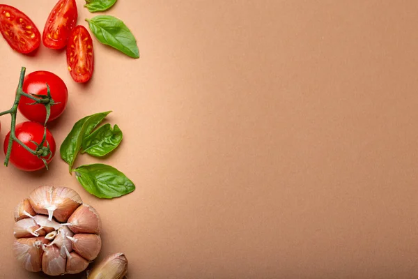 Food cooking border with cherry tomatoes, fresh green basil and garlic cloves top view on simple clean paper background, ingredients for preparing meal, copy space.