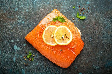 Taze çiğ somon filetosu koyu mavi kırsal beton masa arka planında limon, kaba tuz, yeşil otlar üst manzara. Sağlıklı yemek ve dengeli beslenme.