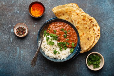 Geleneksel Hint Punjabi yemeği Dal Makhani mercimek ve siyah kasede fasulye bazmati pilavı, naan düz ekmek, taze kişniş ve mavi beton kırsal masa manzaralı kaşık ile servis edilir..