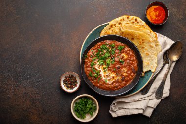 Geleneksel Hint Punjabi yemeği Dal Makhani mercimek ve siyah kasede fasulye ile birlikte naan düz ekmek, taze kişniş ve kahverengi beton kırsal masa manzaralı iki kaşık servis edilir. Metin için boşluk.