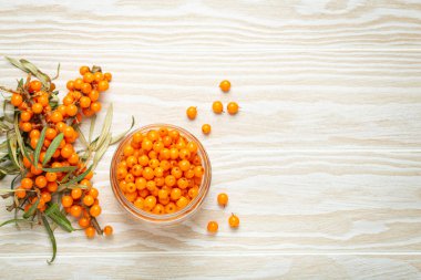 Deniz dikenli üzümler cam kavanozda olgunlaşmış meyveler ve beyaz ahşap arka planda yapraklarla kaplı dallar cilt, kalp, damar ve bağışıklık sistemi için harika..