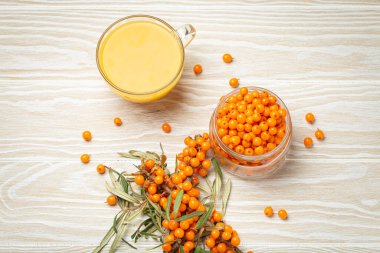 Şeffaf cam fincanda deniz dikenli sağlıklı çay, cam kavanozda olgun böğürtlen ve beyaz ahşap kırsal arka planda yaprakları olan dallar, cilt, kalp, damar ve bağışıklık sistemi için harika...