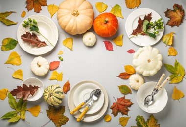 Farklı renkte balkabaklarıyla Şükran Günü şenlik masası kompozisyonu, sonbahar yaprakları, açık gri arka plandaki çatal bıçaklı tabaklar parti ve kutlamaya hazır. Metin için boşluk..
