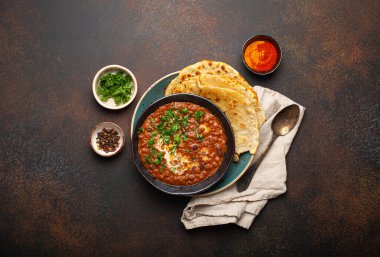 Geleneksel Hint Punjabi yemeği mercimek ve siyah kasede fasulye ile Dal Makhani naan düz ekmek, taze kişniş ve kahverengi beton kırsal masa manzaralı iki kaşık ile servis edilir..