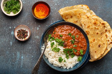 Geleneksel Hint Punjabi yemeği Dal Makhani mercimek ve siyah kasede fasulye bazmati pilavı, naan düz ekmek, taze kişniş ve mavi beton kırsal masa manzaralı kaşık ile servis edilir..