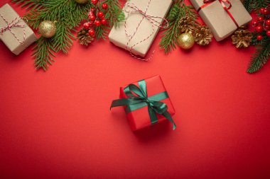 Noel veya Yeni Yıl kutlamaları süsleme ağacı, hediye kutuları, koniler, böğürtlenler, parlak kırmızı toplar ve ortada kırmızı bir hediye ile kırmızı kağıt şenlik arka planı.