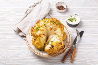 Beyaz ahşap kırsal masa manzaralı, üzerinde zeytin yağı olan kavrulmuş bir baş karnabahar. Vejetaryen yemeği...