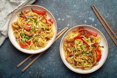 Chow Mein veya Lo Mein ile iki kase, Çin usulü karıştırılmış et ve sebzeli erişte, kırsal mavi beton arka planda çubuklarla servis ediliyor..