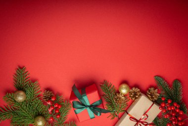 Noel ya da Yeni Yıl kutlamaları kırmızı kağıt şenliği arka planında süsleme köknar ağacı, hediye kutuları, koniler, böğürtlenler, parlak kırmızı toplar. Metin için boşluk..