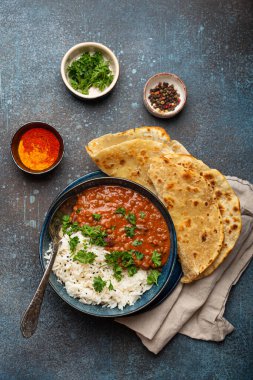Geleneksel Hint Punjabi yemeği Dal Makhani mercimek ve siyah kasede fasulye bazmati pilavı, naan düz ekmek, taze kişniş ve mavi beton kırsal masa manzaralı kaşık ile servis edilir..