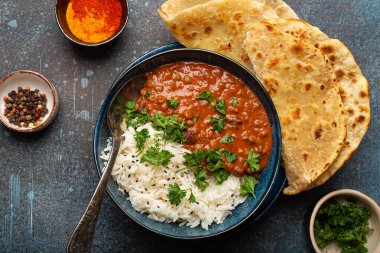 Geleneksel Hint Punjabi yemeği Dal Makhani mercimek ve siyah kasede fasulye bazmati pilavı, naan düz ekmek, taze kişniş ve mavi beton kırsal masa manzaralı kaşık ile servis edilir..