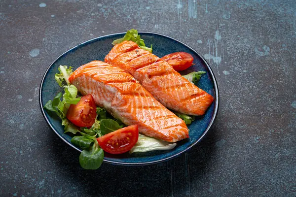 stock image Grilled fish salmon steak with vegetables salad on ceramic plate on rustic stone background angle view, balanced diet or healthy nutrition salad meal with salmon and veggies