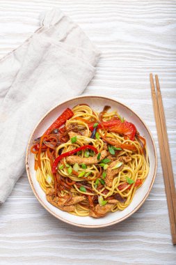 Chow Mein ya da Lo Mein ile beyaz kase, Çin usulü karıştırılmış et ve sebzeli erişte, kırsal beyaz ahşap arka planda çubuklarla servis edilir..