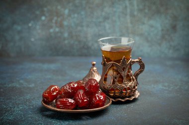 Ramazan ayında kurutulmuş tarihlerle oruç tutmak, tarihli iftar yemeği ve geleneksel bardakta Arap çayı, kırsal mavi arka planda açı manzarası. Müslüman ziyafeti.