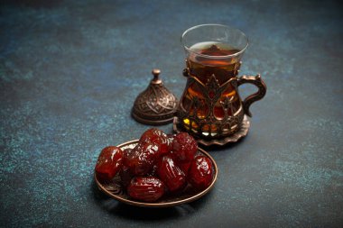 Ramazan ayında kurutulmuş tarihlerle oruç tutmak, tarihli iftar yemeği ve geleneksel bardakta Arap çayı, kırsal mavi arka planda açı manzarası. Müslüman ziyafeti.