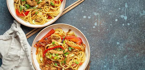 stock image Two bowls with Chow Mein or Lo Mein, traditional Chinese stir fry noodles with meat and vegetables, served with chopsticks top view on rustic blue concrete background, space for text.