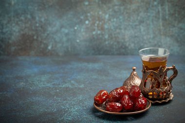 Ramazan ayında kurutulmuş tarihlerle oruç tutmak, tarihli iftar yemeği ve geleneksel bardakta Arap çayı, kırsal mavi arka planda açı manzarası. Müslüman ziyafeti, metin için alan.