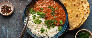 Geleneksel Hint Punjabi yemeği Dal Makhani mercimek ve siyah kasede fasulye bazmati pilavı, naan düz ekmek, taze kişniş ve mavi beton kırsal masa manzaralı kaşık ile servis edilir..