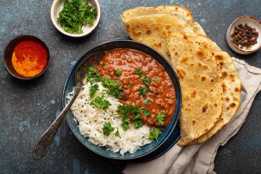 Geleneksel Hint Punjabi yemeği Dal Makhani mercimek ve siyah kasede fasulye bazmati pilavı, naan düz ekmek, taze kişniş ve mavi beton kırsal masa manzaralı kaşık ile servis edilir..
