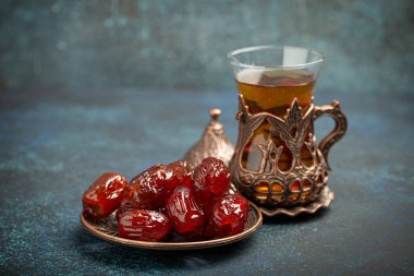 Ramazan ayında kurutulmuş tarihlerle oruç tutmak, tarihli iftar yemeği ve geleneksel bardakta Arap çayı, kırsal mavi arka planda açı manzarası. Müslüman ziyafeti.