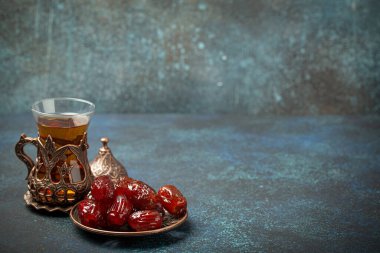 Ramazan ayında kurutulmuş tarihlerle oruç tutmak, tarihli iftar yemeği ve geleneksel bardakta Arap çayı, kırsal mavi arka planda açı manzarası. Müslüman ziyafeti, metin için alan.