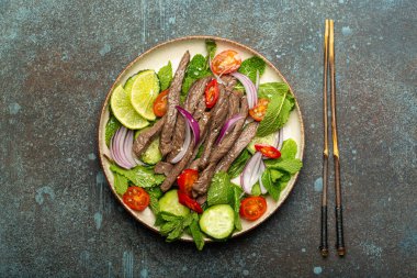 Geleneksel Tayland bifteği salatası, sebzeli ve naneli. Beton kaplama arka planda servis ediliyor. Sağlıklı egzotik Asya yemeği..