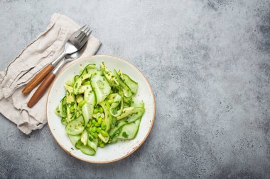 Sağlıklı vejetaryen yeşil avokado salatası kasesi dilimlenmiş salatalıklar, edamame fasulyeleri, zeytinyağı ve seramik tabakta bulunan otlar gri taş kırsal masa arka planında. Metin için boşluk