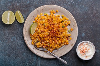 Meşhur bir Meksika sokak yemeği olan esquites tabağı limon dilimleri ve acı biberli ekşi kremayla servis edilir.