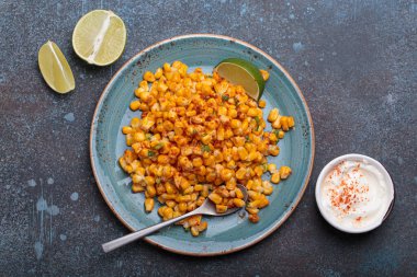 Meşhur bir Meksika sokak yemeği olan esquites tabağı limon dilimleri ve acı biberli ekşi kremayla servis edilir.