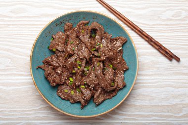 Lezzetli bulgogi tabağı. Beyaz ahşap arka planda ızgara salamura edilmiş sığır eti içeren geleneksel Kore yemeği.