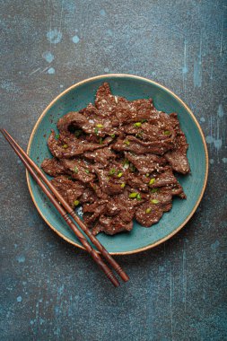 Lezzetli bir bulgogi tabağı, geleneksel Kore yemeği. Tabakta terbiye edilmiş et ve yemek çubukları var.