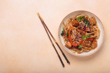 Susam tohumu ve maydanozla süslenmiş bir kase lezzetli udon eriştesi yemek çubukları ve limon dilimleri ile bej bir masada servis ediliyor. Metin için boşluk