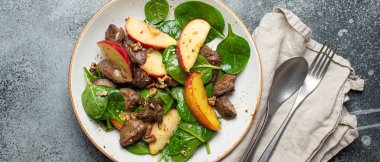 Demir zengini tavuk ciğeri, elmalar, taze ıspanak ve cevizli beyaz seramik tabak, gri taştan arka plan manzaralı sağlıklı salata..