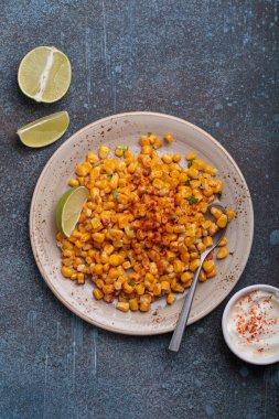 Meşhur bir Meksika sokak yemeği olan esquites tabağı limon dilimleri ve acı biberli ekşi kremayla servis edilir.