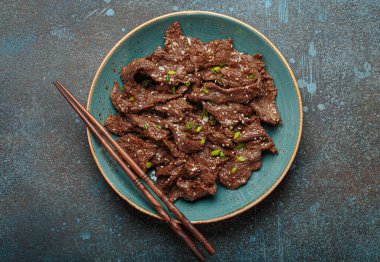 Lezzetli bir bulgogi tabağı, geleneksel Kore yemeği. Tabakta terbiye edilmiş et ve yemek çubukları var.