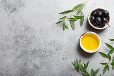 Siyah zeytin ve ekstra saf zeytin yağı küçük bir kasede zeytin dalları gri beton arka planda üst görünüm, metin için boşluk