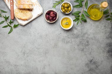 Kesme tahtasında dilimlenmiş taze ciabatta, yeşil ve kahverengi zeytinler, biberiyeli zeytin yağı, gri beton taş kırsal arka plan manzaralı zeytin ağacı dalları, kopyalanmış uzay sınırı