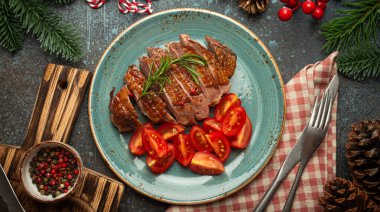 Dilimlenmiş ördek göğsü filetosu, altın çıtır deri ve domates salatası, köknar ağacı, koni, kırmızı böğürtlen, mavi kırsal beton arka planlı Noel süslemeleri...