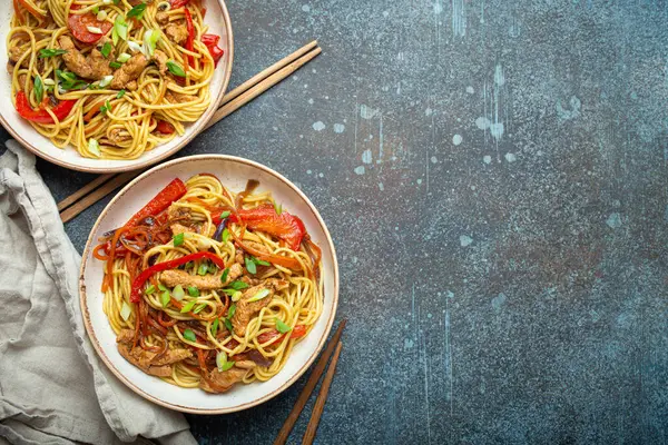 stock image Two bowls with Chow Mein or Lo Mein, traditional Chinese stir fry noodles with meat and vegetables, served with chopsticks top view on rustic blue concrete background, space for text.