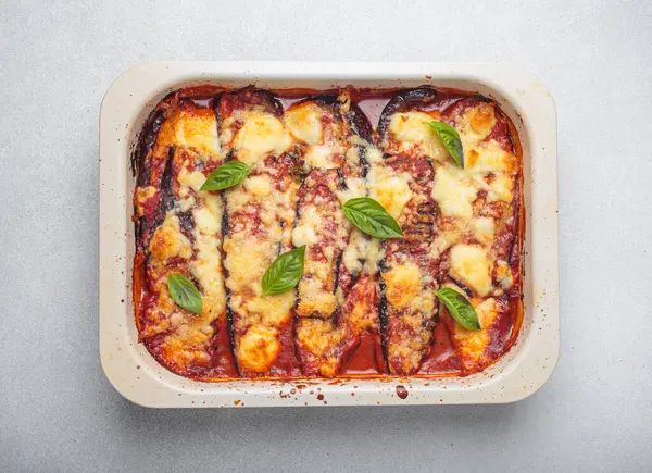 stock image Eggplant parmigiana di melanzane freshly baked and decorated with basil leaves, resting in a baking pan. Classic italian dish