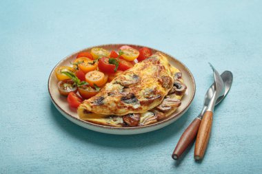 Sağlıklı kahvaltı ya da yukarıdan öğle yemeği için taze kiraz domatesli ve mavi arka planda fesleğenli kızarmış mantarlı leziz omlet.