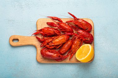 Tahta kesme tahtasının üzerinde birkaç kırmızı kerevit ve mavi dokulu arka planda yukardan çekilmiş bir dilim limon var.