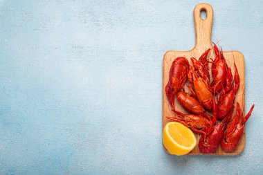 Tahta bir kesme tahtasının üzerinde birkaç kırmızı kerevit ve bir dilim limon, yukarıdan mavi dokulu bir arka planda çekilmiş, metin için boşluk