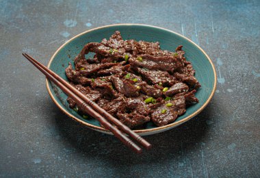 Lezzetli bir bulgogi tabağı, geleneksel Kore yemeği. Tabakta terbiye edilmiş et ve yemek çubukları var.