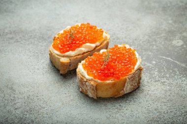 İki havyar ekmek kızartması, tereyağı ve kırmızı somon havyarlı, gri beton arka plan, şenlikli lüks lezzet ve aperatif..