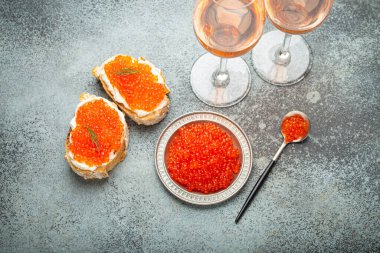 Kırmızı somon havyarlı küçük metal tabak, iki havyar tostu kanepesi, gri beton arka planda iki bardak şampanya, şenlikli lüks lezzet ve aperatif..