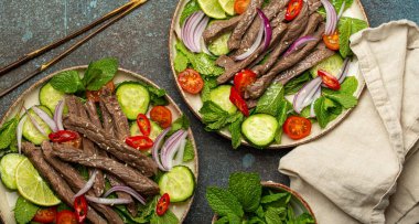 İki tabak geleneksel Tayland sığır eti salatası, sebzeli ve naneli. Beton arka planda servis ediliyor, sağlıklı egzotik Asya yemeği..