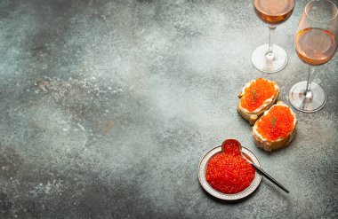 Kırmızı somon havyarlı küçük metal tabak, iki havyar tostu, gri beton arka planda iki bardak şampanya, şenlikli lüks lezzet ve aperatif. Metin için boşluk